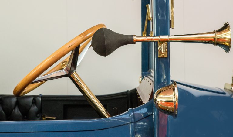 The front of a vintage blue car with an antique golden steering wheel and a separate horn